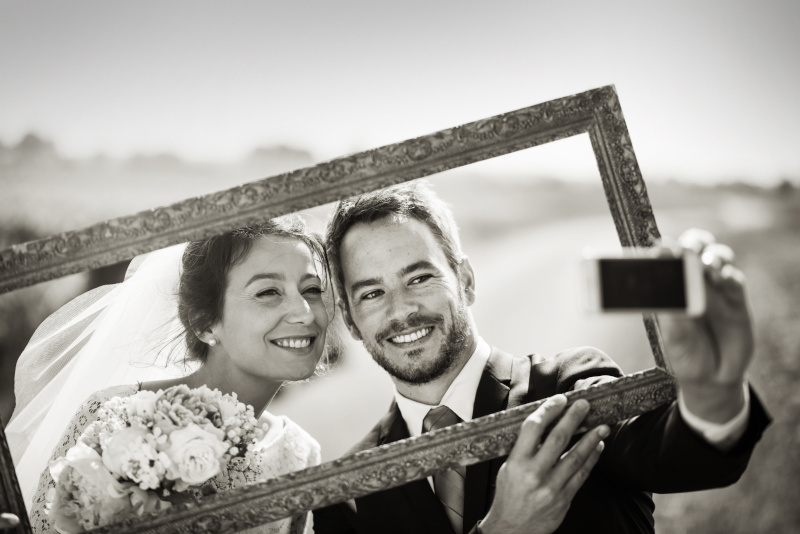Ein junges Brautpaar hält einen Bilderrahmen vor sich und macht ein Selfie.