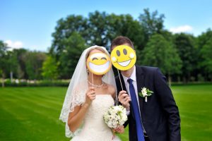 Braut und Bräutigam halten sich Pappschilder mit breitem Lächeln vor ihr Gesicht.